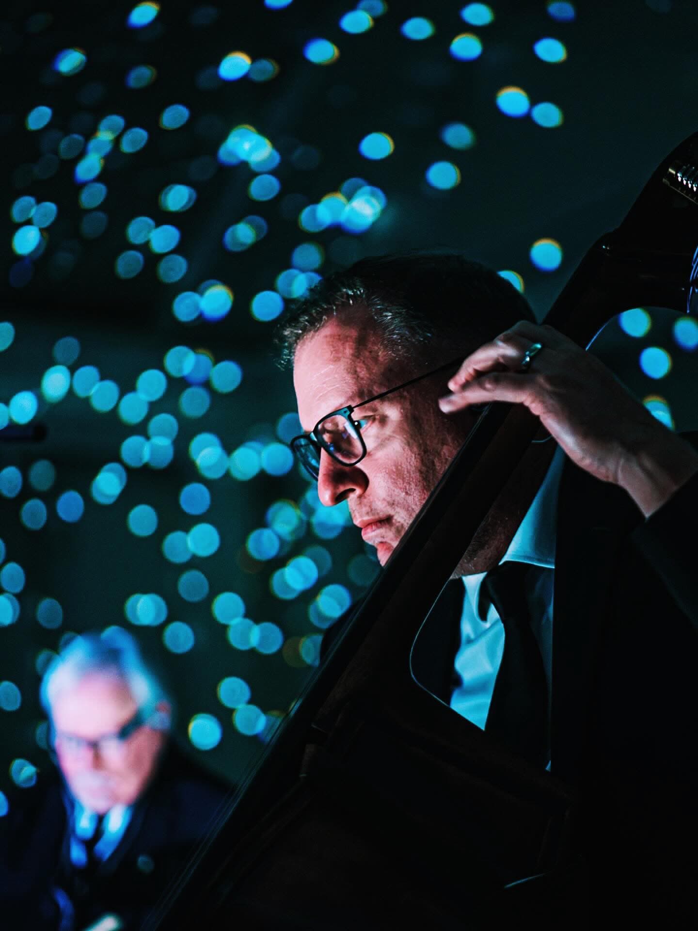 The bassist leaning into an upright bass against a wall of blue stars